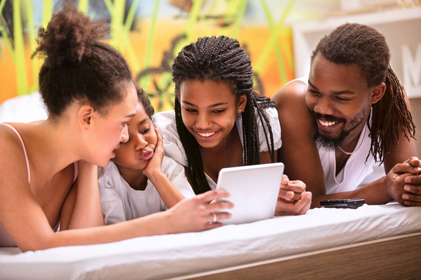 Famille afro-américaine avec enfants dans la chambre à coucher regardant écran de tablette ensemble
 - Photo, image