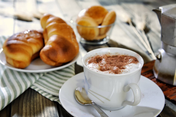 Traditioneel Italiaans ontbijt met cappuccino en croissants op een rustieke houten tafel - Foto, afbeelding