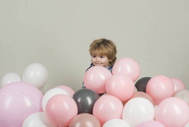 Meglepetés. Bújócska a gyermekek körül a lufi. Kis gyerek elrejti a színes ballonok. Gyermek aranyos mosollyal elrejti a rózsaszín, szürke és fehér léggömbökkel. Gyerek születésnapi dekoráció - Fotó, kép