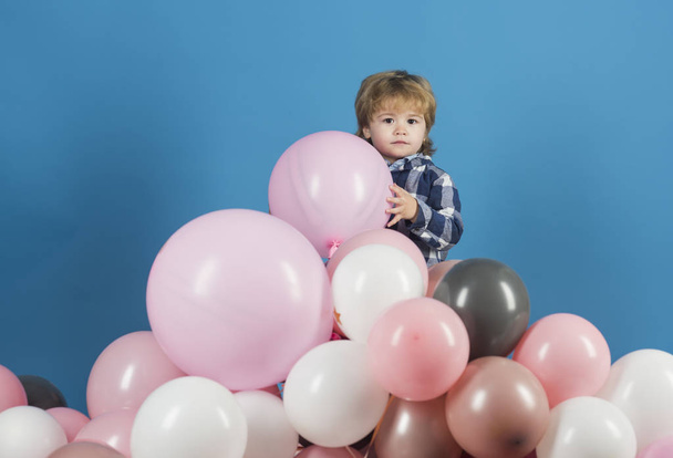 Boy kid and mountain of pink balloons, birthday holiday or opening new children shop or kindergarten. Game and good mood, child holding keeps ball toy. Cute boy with long hair played in playground - Photo, Image