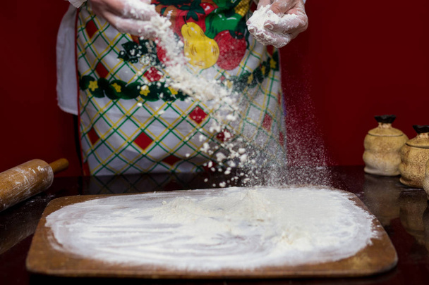 Una mujer cocina rociando harina sobre una tabla de cortar. Cocinar. Hacer pan en la mesa de la cocina. Concepto de proceso de cocina
 - Foto, Imagen