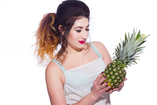 Summer studio portrait of a beautiful young brunette woman with long hair. A girl in a summer T-shirt and jeans is holding a pineapple in her hands. Concept: summer photography and a sunny mood - Photo, Image
