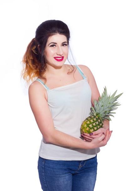 Summer studio portrait of a beautiful young brunette woman with long hair. A girl in a summer T-shirt and jeans is holding a pineapple in her hands. Concept: summer photography and a sunny mood - Foto, immagini