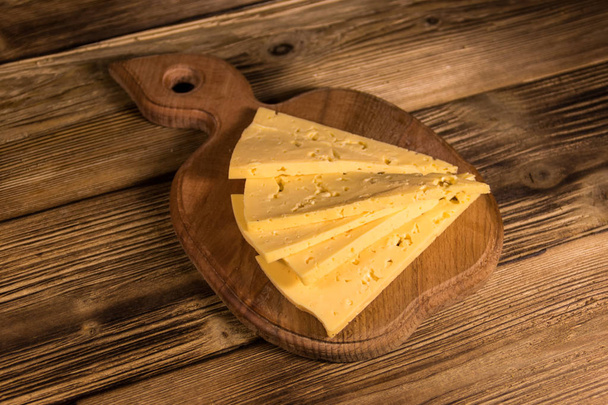 Plakjes kaas op de snijplank op houten tafel - Foto, afbeelding