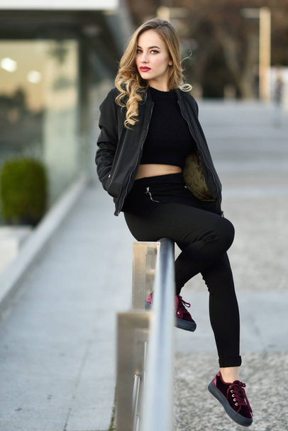 Beautiful young girl wearing black jacket sitting in the street. - Φωτογραφία, εικόνα