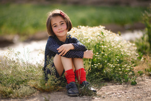 Μικρό κορίτσι που κάθεται στο πεδίο φύση φοράει όμορφο φόρεμα - Φωτογραφία, εικόνα