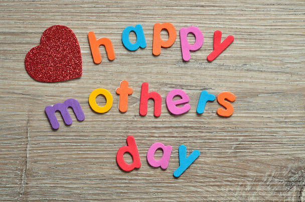 Happy mothers day in colorful letters on a wooden background with a red heart - Fotografie, Obrázek