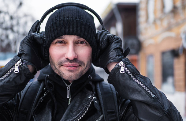 Lächelnder Mann, der auf der Winterstraße läuft und über Kopfhörer Musik hört - Foto, Bild