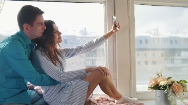 Gelukkig vrolijke verliefde paar maken selfie op venster, jonge aantrekkelijke jongen en meisje - Video