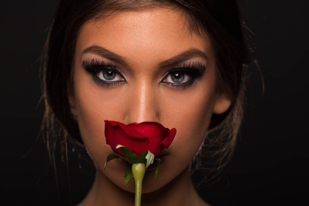 Beautiful young woman smelling a rose closeup beauty looking into the camera - Fotó, kép
