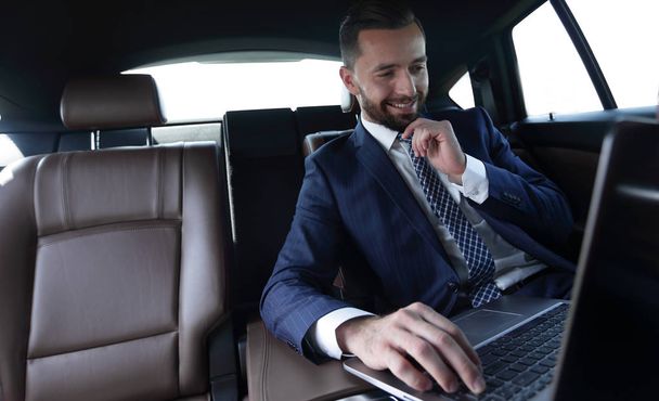 businessman reads information on laptop while sitting in car - Fotó, kép