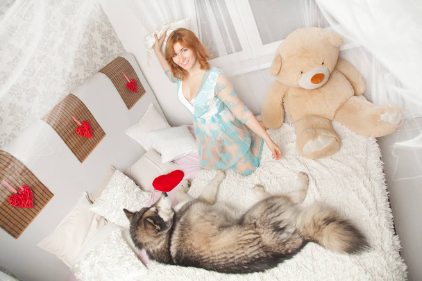 beautiful european girl is lying and sleeping in lace nightgown with her best friend dog Malamute in white bed top view - Photo, Image