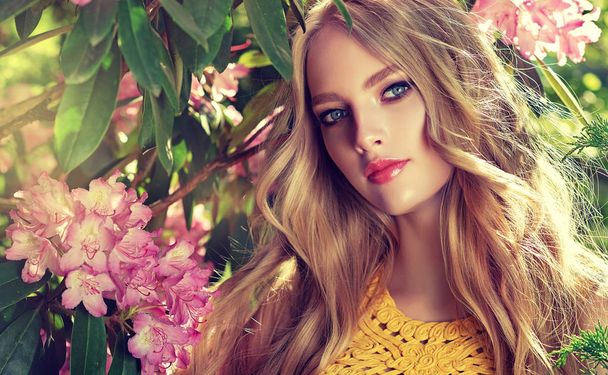 夏の花公園で香りのよい花の美しい春モデルの女の子。ブルーミング ガーデンの女性。ファッション、化粧品・香水。金髪巻き毛 - 写真・画像
