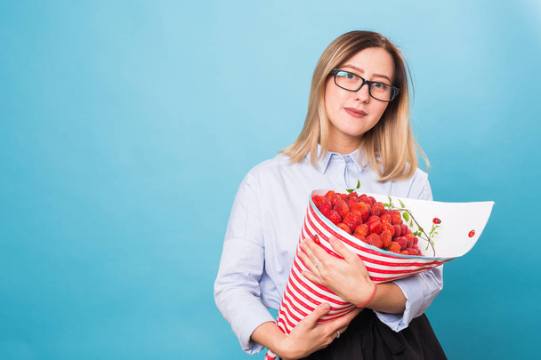 Strauß Erdbeeren in den Händen eines Mädchens auf blauem Hintergrund - Foto, Bild