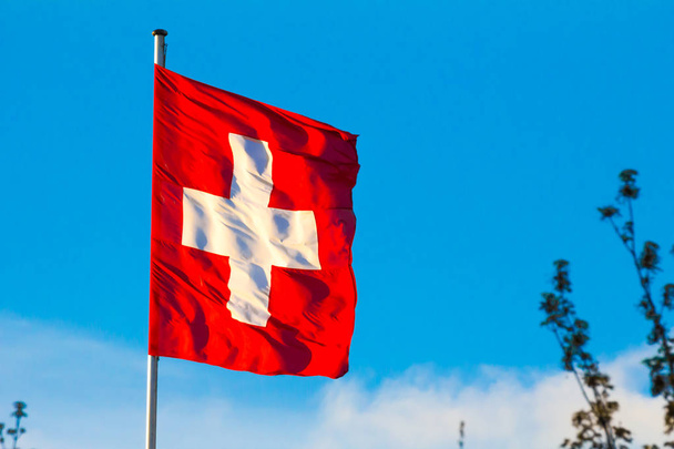 Confederação Suíça, bandeira nacional da Suíça acenando no fundo do céu azul
 - Foto, Imagem