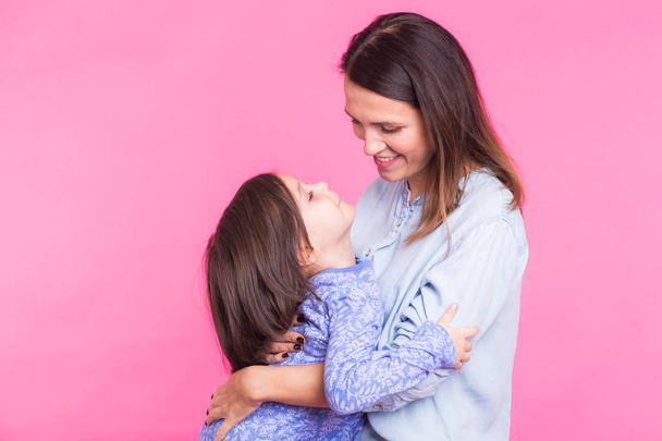 Menschen, Glück, Liebe, Familie und Mutterschaft Konzept - glückliche kleine Tochter umarmt und küsst ihre Mutter vor rosa Hintergrund - Foto, Bild