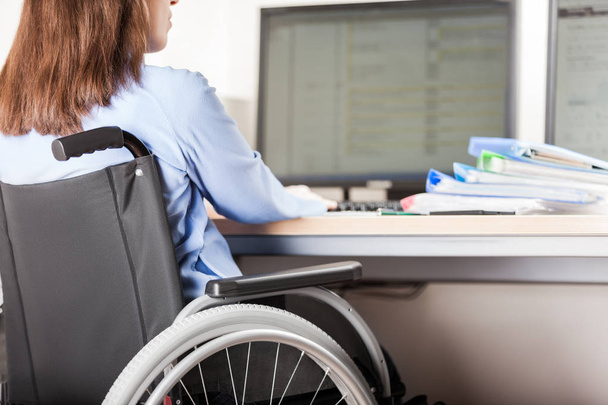 Invalid or disabled woman sitting wheelchair working office desk computer - Foto, immagini