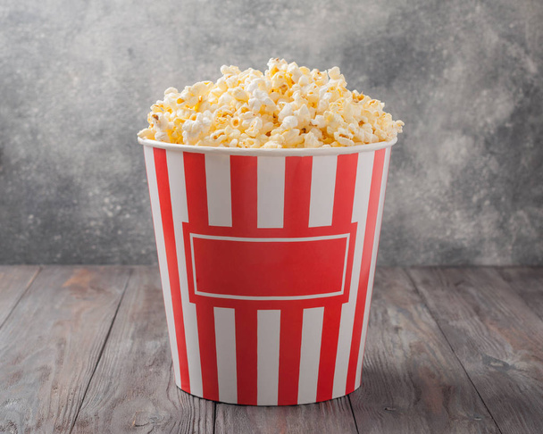 Popcorn in einem gestreiften Eimer (rot-weiße Schachtel) isoliert auf grau - Foto, Bild