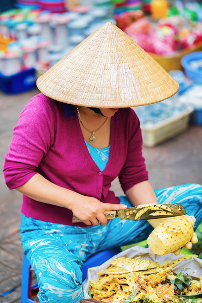 Азиатская женщина режет ананас на уличном рынке в Кантхо
 - Фото, изображение