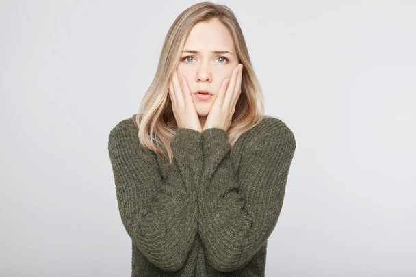 Strach strach blond žena nosí zelený svetr, vypadá s vyděšeným výrazem ve tváři, strach něco, vyjadřuje negativní emoce a pocity, představuje proti bílým pozadím doma ve studiu. - Fotografie, Obrázek