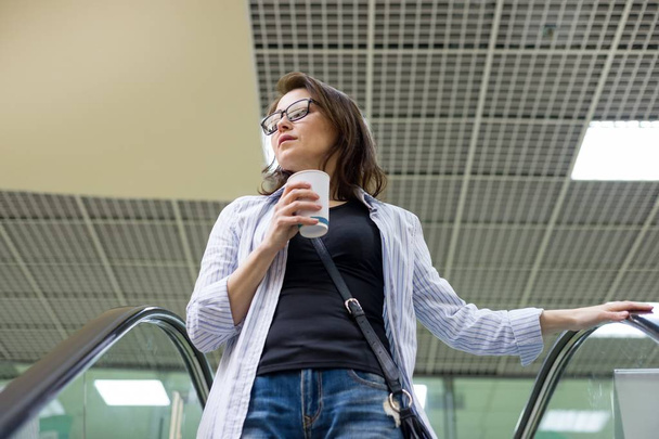 Middle-aged woman with a cup of coffee, background shopping mall entertainment center. - Foto, Imagen