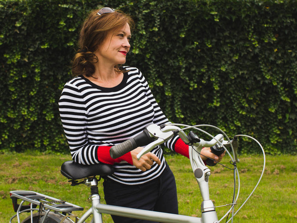 Portrait of a middle aged woman smiling leaning on a bicycle. - Photo, Image