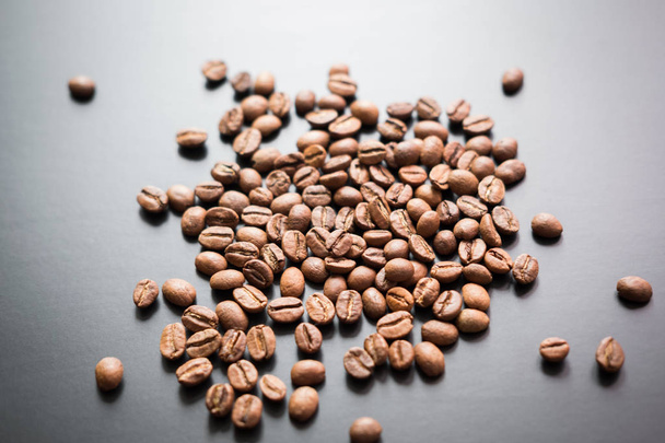 The grains of roasted coffee are scattered on a black matte surface - Photo, image