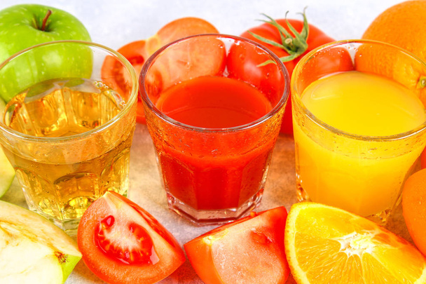 新鮮なオレンジ、リンゴ、トマト ジュースの灰色のコンクリート表とメガネ。小葉の果物や野菜. - 写真・画像