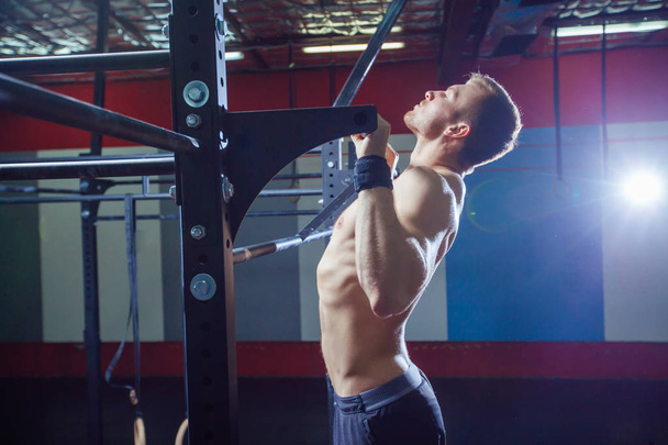 Athlete muscular fitness male model pulling up on horizontal bar in a gym. Crossfit style - Foto, Imagen