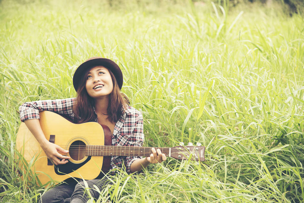 Belle jeune femme jouant de la guitare sur la prairie verte
. - Photo, image