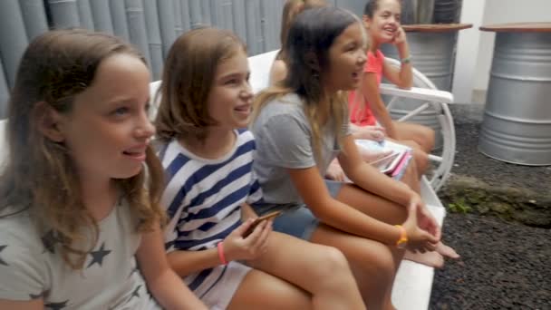 Zróżnicowaną grupę szczęśliwy dziewcząt siedzieli na ławce - Materiał filmowy, wideo
