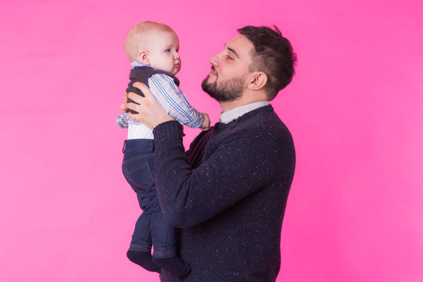Happy father holding baby son in hands over pink background - Zdjęcie, obraz