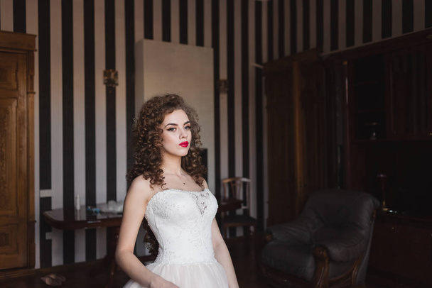 beautiful bride is standing in a room by the window - Фото, изображение