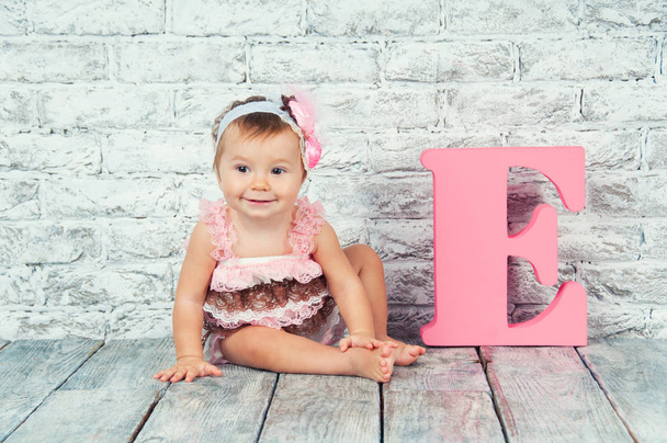 Beautiful and cute girl in pink dress with the letter E. Emotional girl. - Foto, imagen
