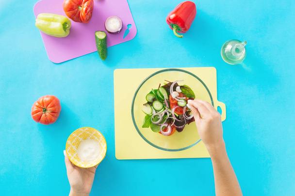 Healthy food concept. Diet food. Female hands prepare summer vegetarian salad on blue background - Photo, image