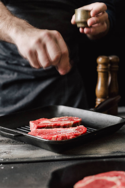 Chef sprinkle salt beef steaks on kitchen. Man cooking beef steaks - Фото, зображення