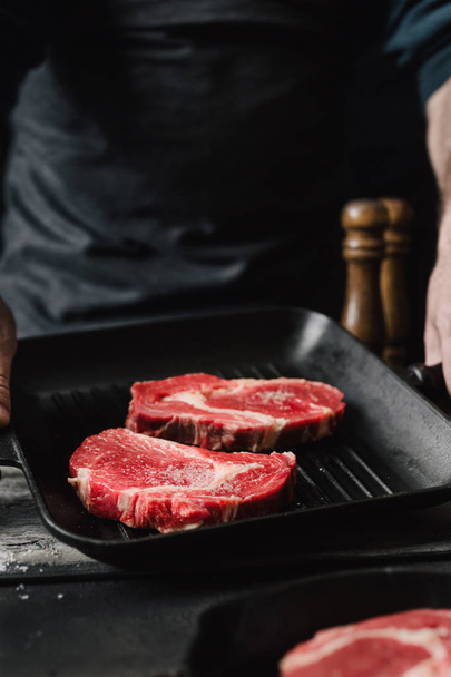 Mužské ruce držící gril pánev s hovězí steaky v kuchyni člověk vaření hovězí steaky - Fotografie, Obrázek