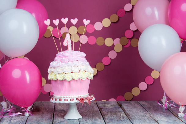 First birthday cake with a unit on a pink background with balls and paper garland. - Фото, зображення