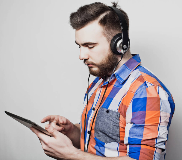 Studio portrait of a handsome bearded man using a tablet with headphones over a light grey  background. - Foto, immagini