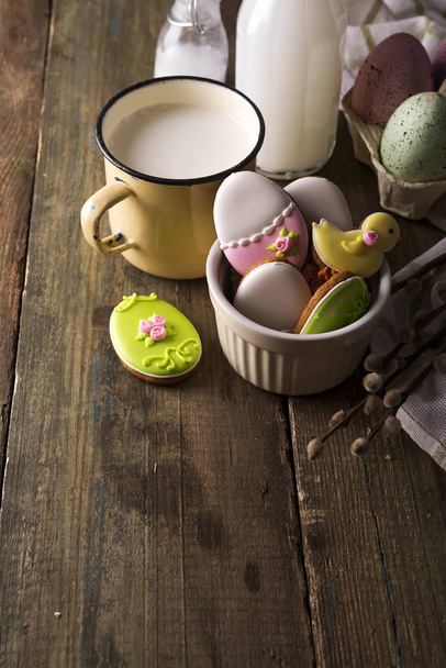 Plaat met kleurrijke Pasen koekjes en glas melk, rustieke stijl - Foto, afbeelding