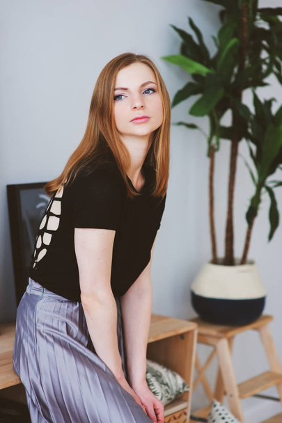 young woman posing at home in modern interior in metallic grey skirt and black top - Foto, afbeelding