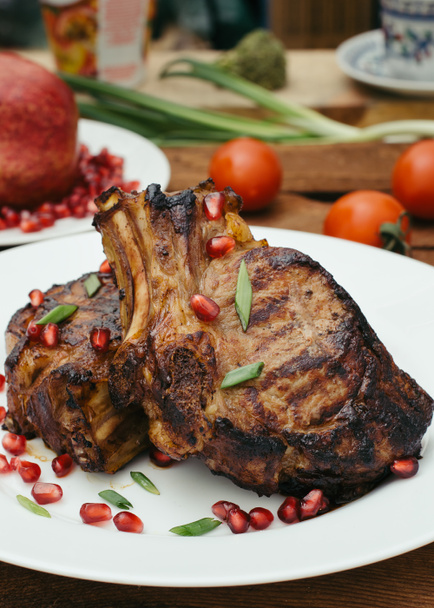 Biefstuk op ribs, gekookt op een grill met granaatappel op een witte plaat. Houten rustieke achtergrond. Bovenaanzicht - Foto, afbeelding