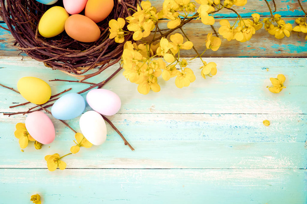 Colorful Easter eggs in nest with flower on rustic wooden planks background in blue paint. Holiday in spring season. vintage color tone style. top view composition. - Fotografie, Obrázek