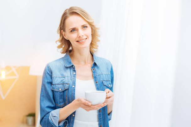 Calm pleasant woman looking peaceful while standing with a cup of tea - Photo, Image