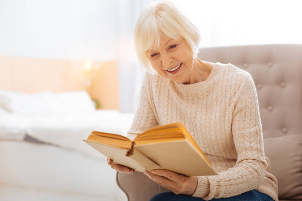 Pleasant kind aged woman smiling and reading a lovely book - Zdjęcie, obraz