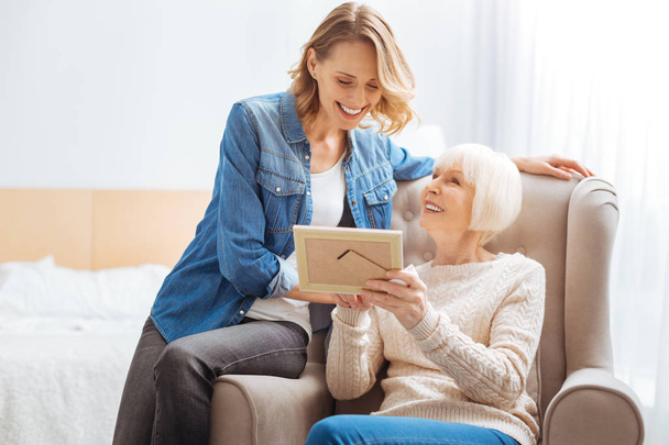 Happy elderly woman smiling while showing a photo to her granddaughter - Fotoğraf, Görsel