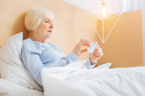 Konzentrierte ältere Frau mit einer Pillbox im Bett - Foto, Bild