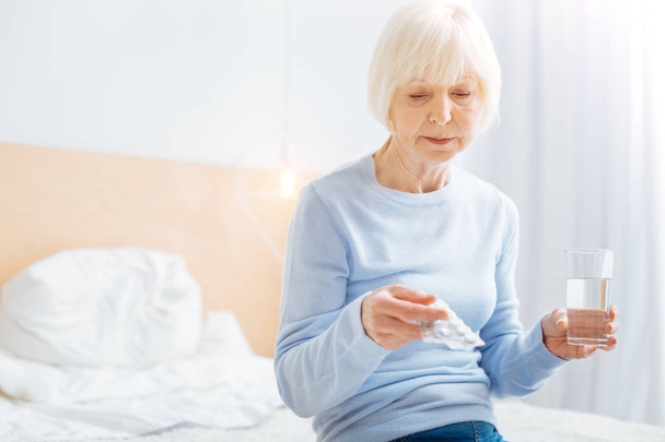 Tired pensioner taking pills while feeling bad ad sitting at home - Foto, Bild