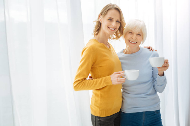 Positivos parientes lindos abrazando y sonriendo mientras beben su té
 - Foto, imagen