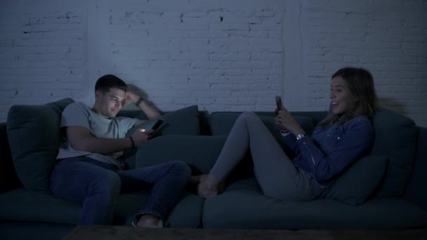 panning shot of young man using mobile phone relaxed on couch with his girlfriend when she receives a phone call and gets happy and excited starting a video feed , the boyfriend getting jealous and moody - Πλάνα, βίντεο